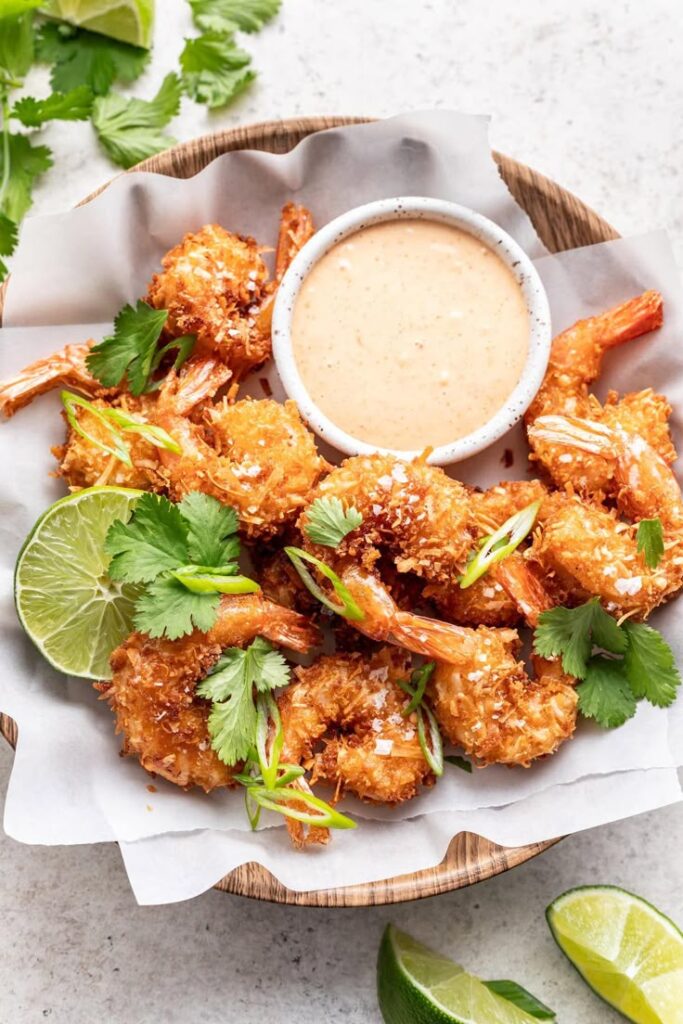 Crispy Coconut Shrimp with Sweet Chili Sauce - Well Seasoned Studio - Crispy Coconut Shrimp & Sweet Chili Sauce Recipe Crispy coconut shrimp with lime and spicy dipping sauce, garnished with cilantro in a wooden bowl.