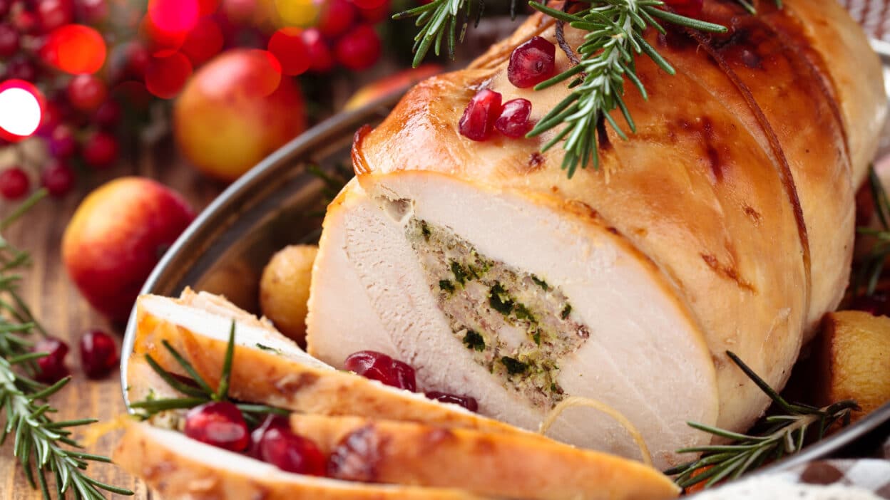 Roasted stuffed turkey breast garnished with rosemary and pomegranate seeds, perfect for holiday feasts.