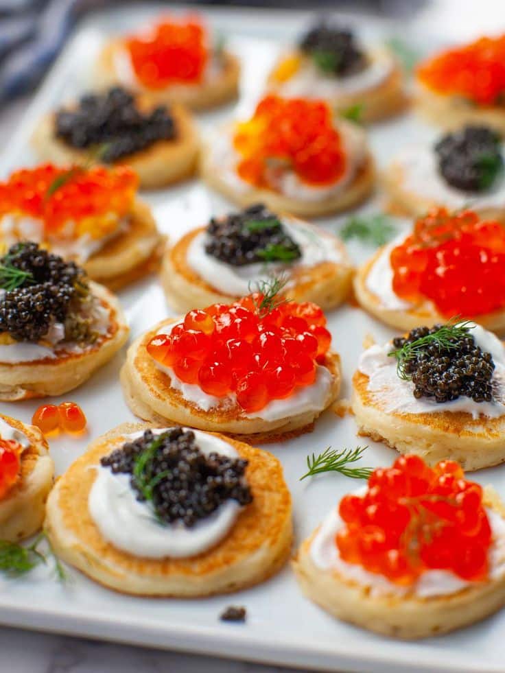 Easy Blini with Caviar video - Elegant Caviar Party Bites for New Year's Eve Assorted blinis topped with red and black caviar and cream, garnished with fresh dill on a serving platter.