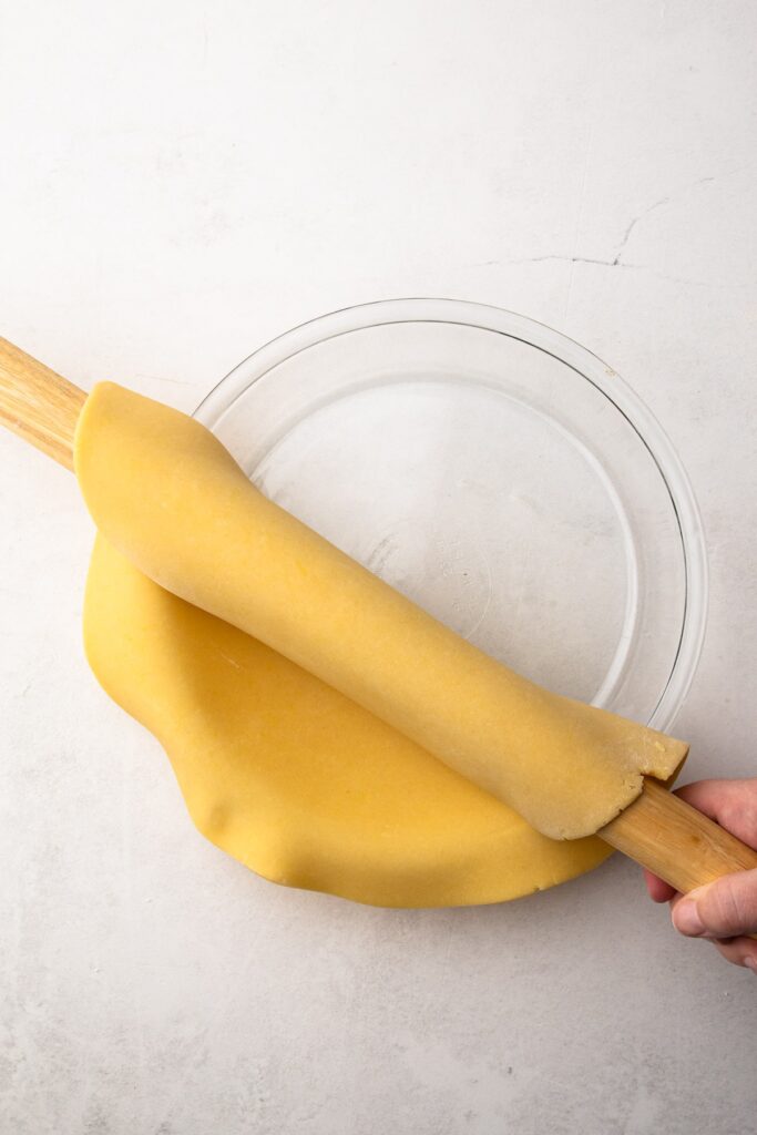 French-Silk-Pie-1 - Delicious Pistachio Pie Ideas for Parties and Holidays Rolling out pie crust dough over a glass pie dish with a wooden rolling pin.