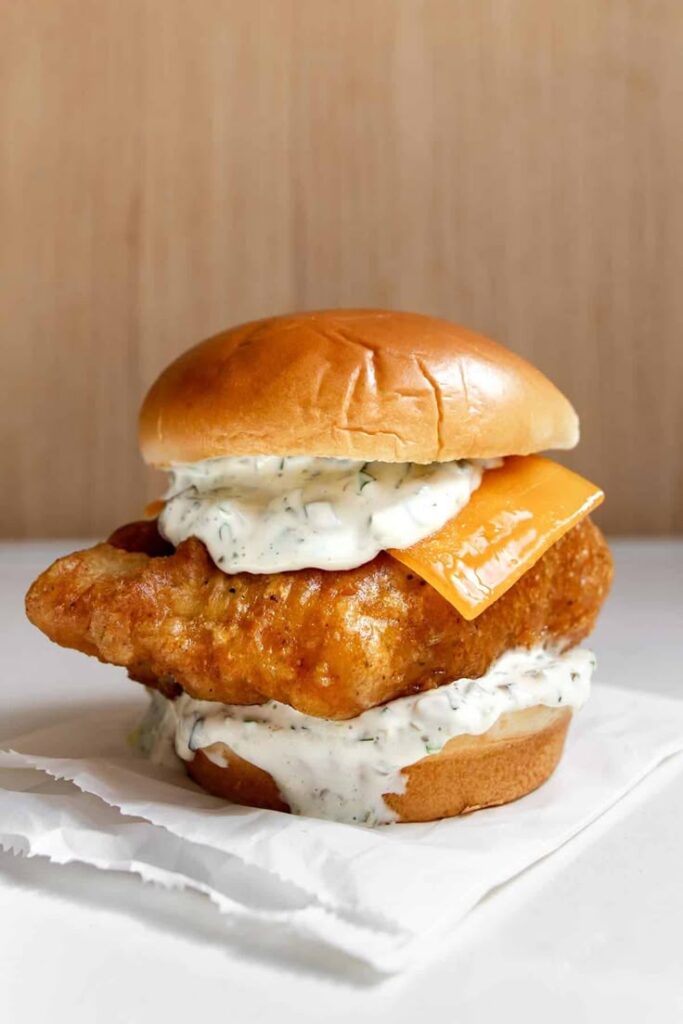 Crispy fish sandwich with tartar sauce and cheese on a soft bun, perfect for seafood lovers.