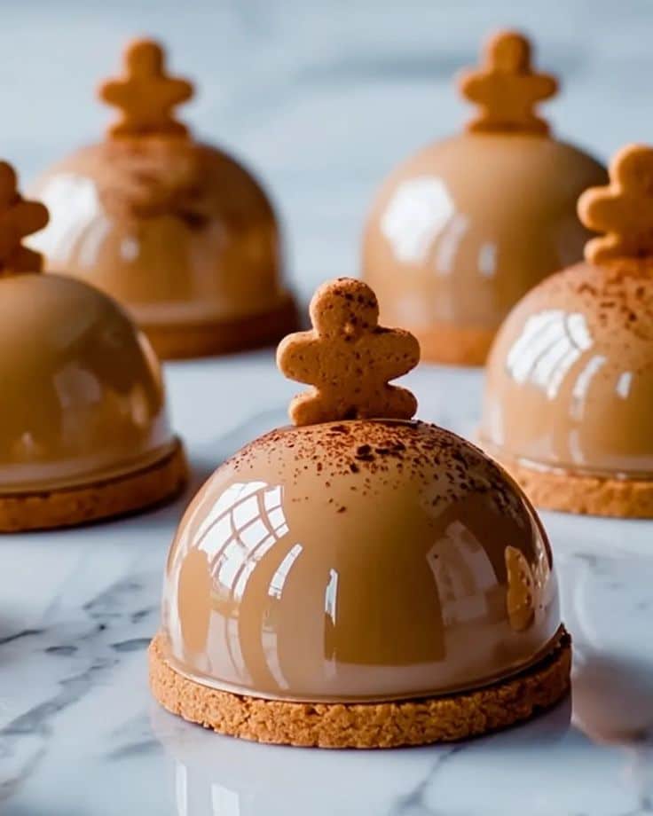 Gingerbread Latte Mousse Domes_ 5 Delicious Holiday Layers - Gingerbread Latte Mousse Domes Recipe | Chief Stories Decorative caramel domes topped with gingerbread cookies on a marble surface, reflecting natural light. Gingerbread Latte Mousse Domes