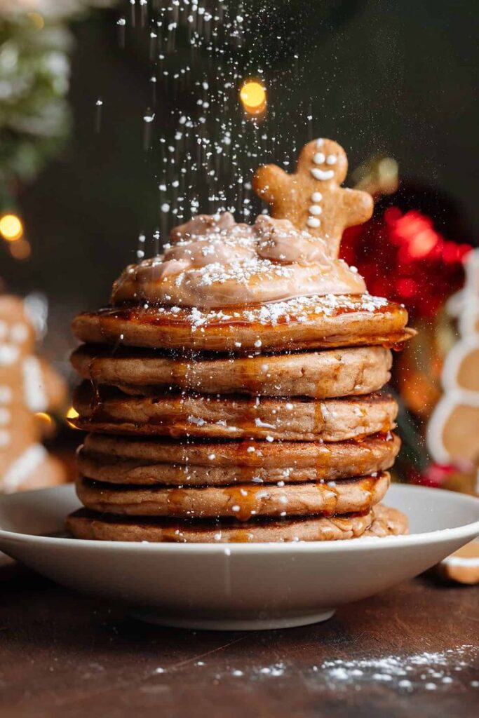 Gingerbread Pancakes - Gingerbread Pancakes Recipe | Cozy Holiday Breakfast Stack of pancakes topped with gingerbread man and syrup, dusted with powdered sugar, festive holiday background.