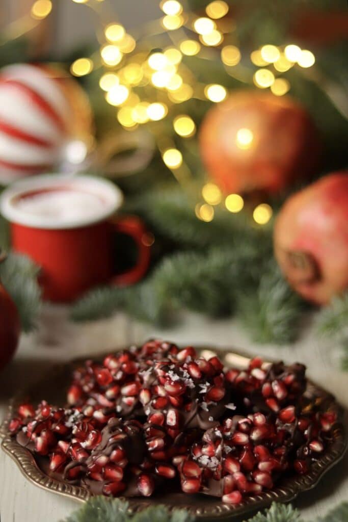 Granatäppelgodis - Festive & Easy: Master the Perfect Pomegranate Paloma Festive chocolate-covered pomegranate on a plate with holiday lights and decor.