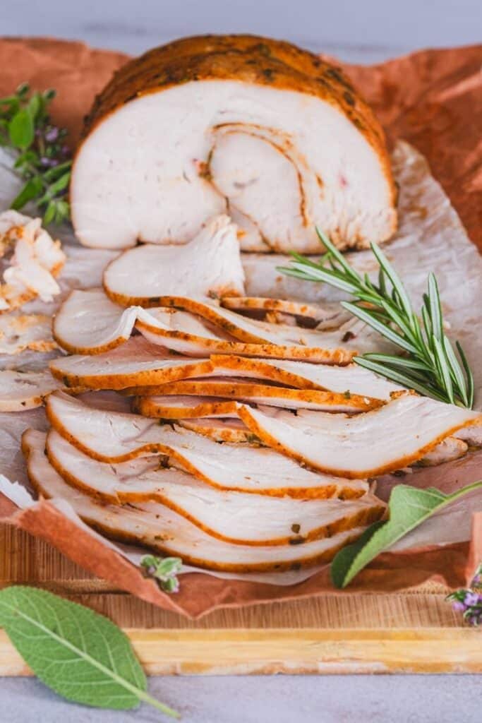 Sliced roasted turkey breast with herbs on wooden board, perfect for a festive meal or healthy dinner.