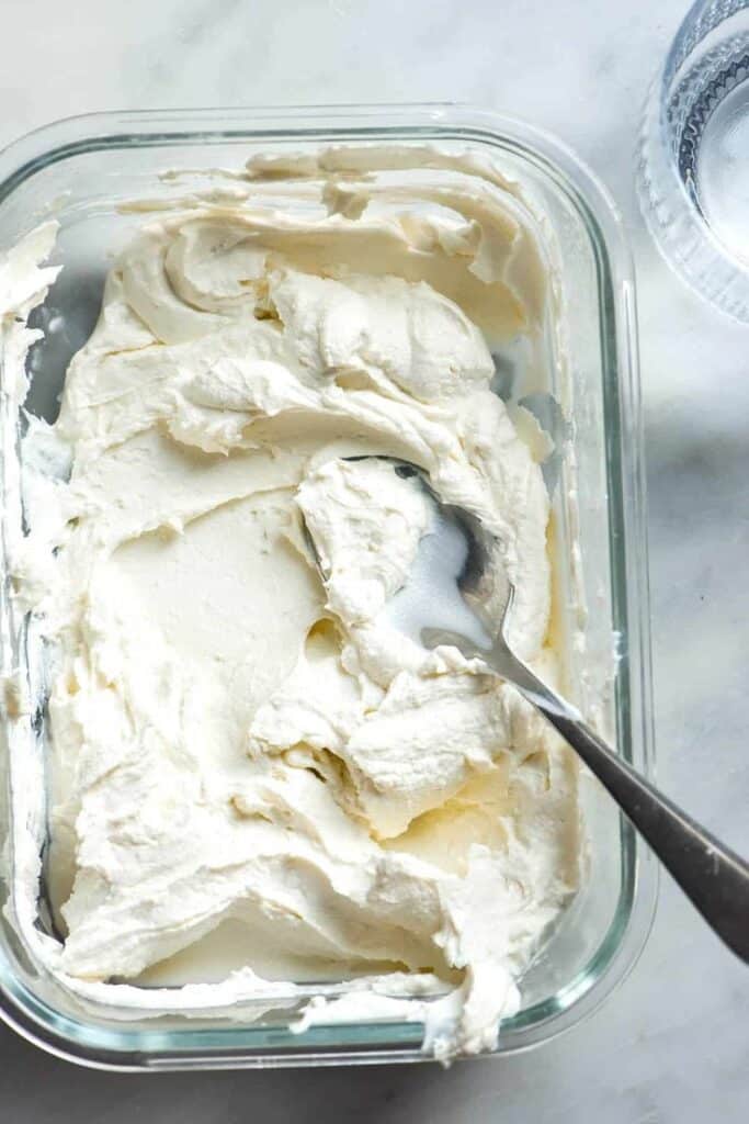 Creamy whipped cream cheese in a glass container with a spoon, perfect for spreading on bagels or baked goods.