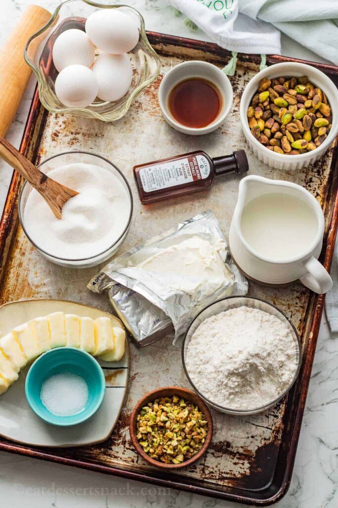 Pistachio-Custard-Pie-Ingredients - Delicious Pistachio Pie Ideas for Parties and Holidays Baking ingredients flat lay: eggs, flour, sugar, milk, vanilla, butter, cream cheese, pistachios for desserts.