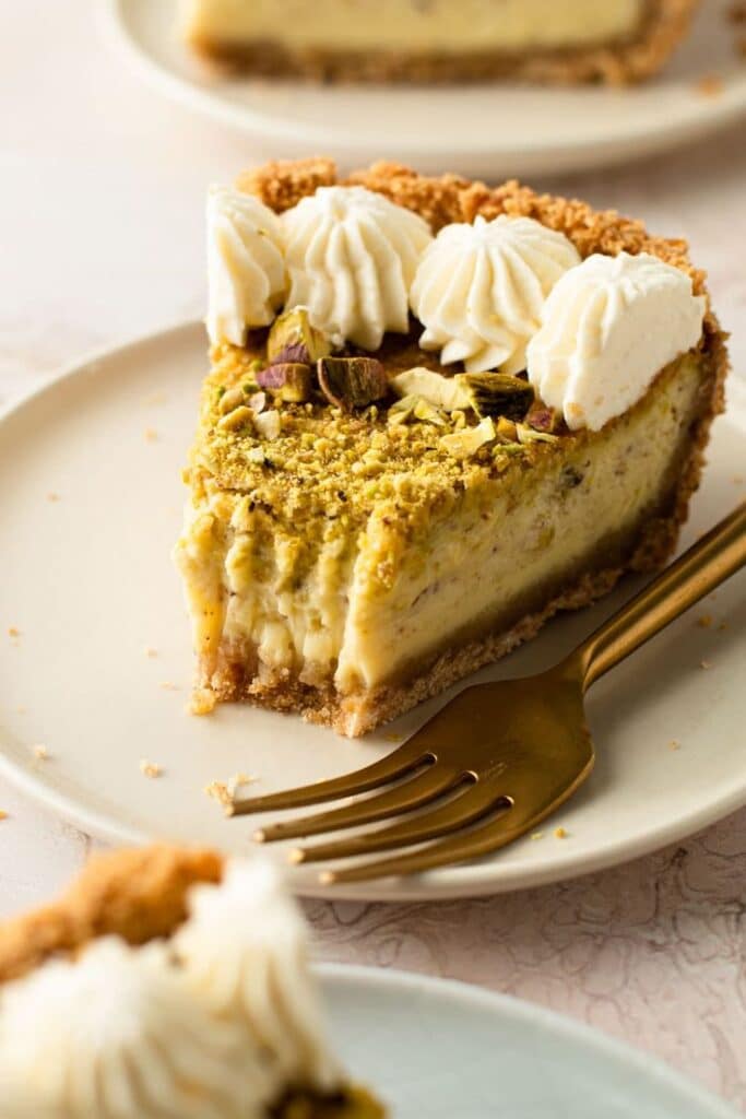 Pistachio Pie with Mascarpone in a Pretzel Crust - Everyday Pie - Delicious Pistachio Pie Ideas for Parties and Holidays Slice of creamy pistachio cheesecake topped with whipped cream on a plate with a fork.