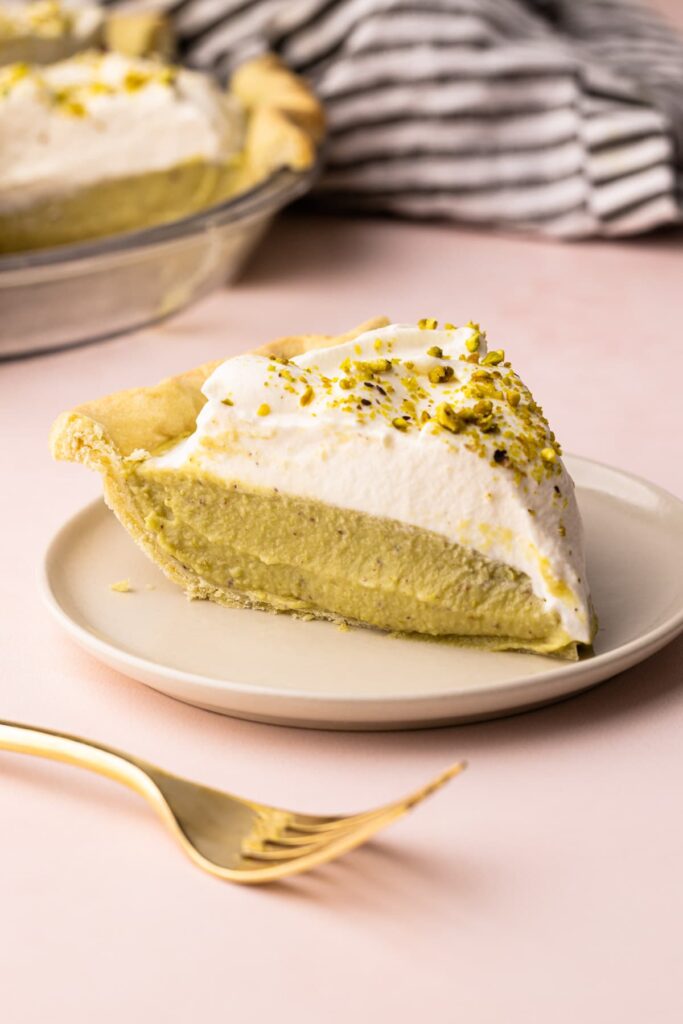 Pistachio-cream-pie-23 - Delicious Pistachio Pie Ideas for Parties and Holidays Slice of creamy pistachio pie topped with whipped cream and crushed pistachios on a plate.