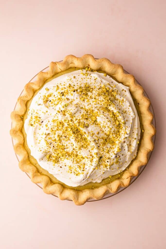 Pistachio-cream-pie-41 - Delicious Pistachio Pie Ideas for Parties and Holidays Creamy pistachio pie topped with whipped cream and crushed pistachios on a soft pink background.