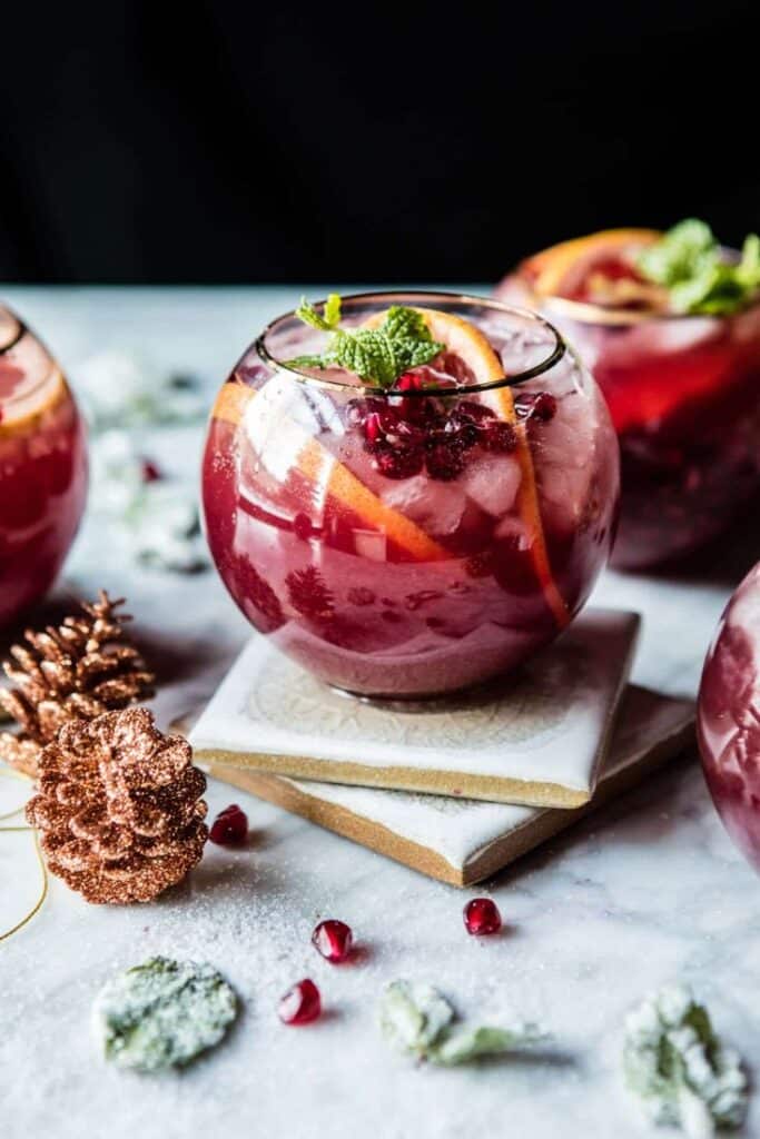 Pomegranate Ginger Paloma_ - Festive & Easy: Master the Perfect Pomegranate Paloma Festive pomegranate cocktail with orange slices and mint in a round glass on a marble table, perfect for holiday celebrations.