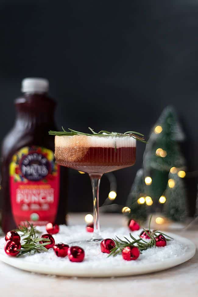 Snowy Poinsettia Martini - Snowy Poinsettia Martini: Your Ultimate Holiday Cocktail Festive punch cocktail in a glass, garnished with rosemary, with bottle in background and holiday decorations. Snowy Poinsettia Martini