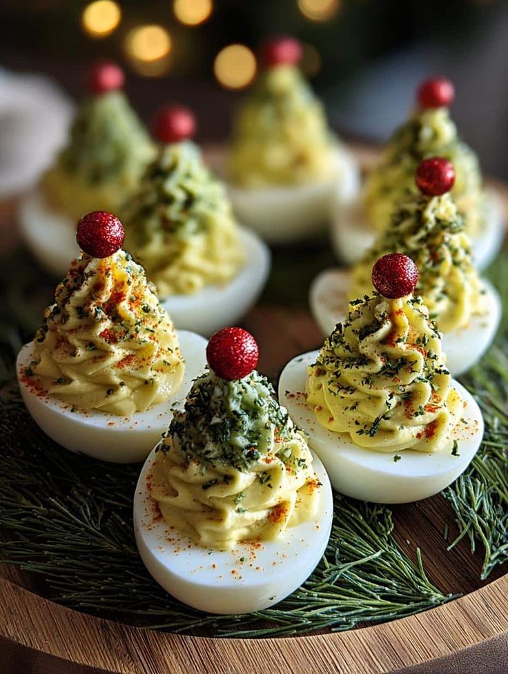 Festive deviled eggs styled as Christmas trees with herbs and red toppings on a wooden platter with green garnish.