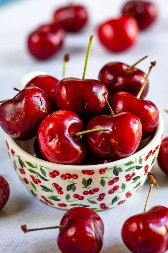 Fresh red cherries in a decorated bowl with cherry pattern, ideal for healthy summer snacks.