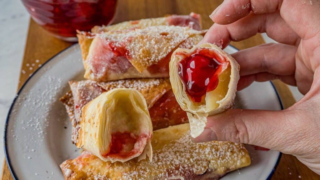 Flaky pastry rolls filled with vibrant red jelly, dusted with powdered sugar, on a white plate.