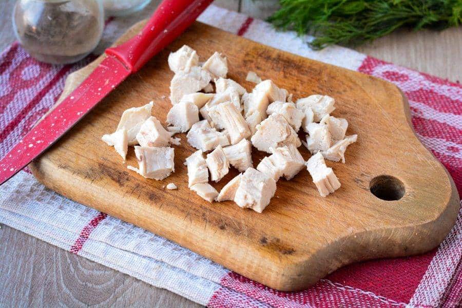 salat_s_kuricei_yablokami_i_orehami-636363 - Make Delicious Chicken Salad with Walnuts & Cheese in Minutes Diced chicken on a wooden cutting board with a red knife, ready for cooking on a red and white kitchen towel.