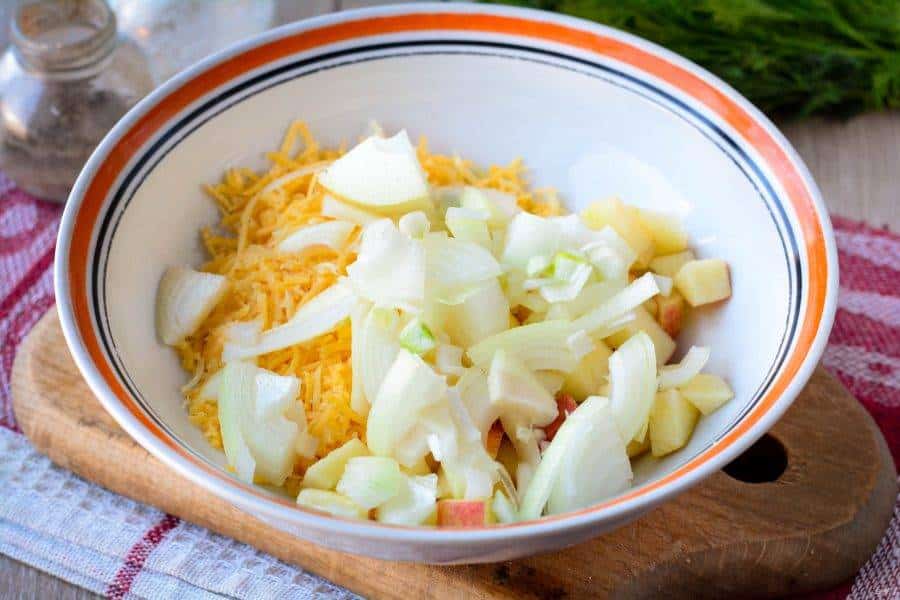 salat_s_kuricei_yablokami_i_orehami-636368 - Make Delicious Chicken Salad with Walnuts & Cheese in Minutes Bowl of chopped onions, apples, and shredded cheese on a wooden board, ready for salad preparation.