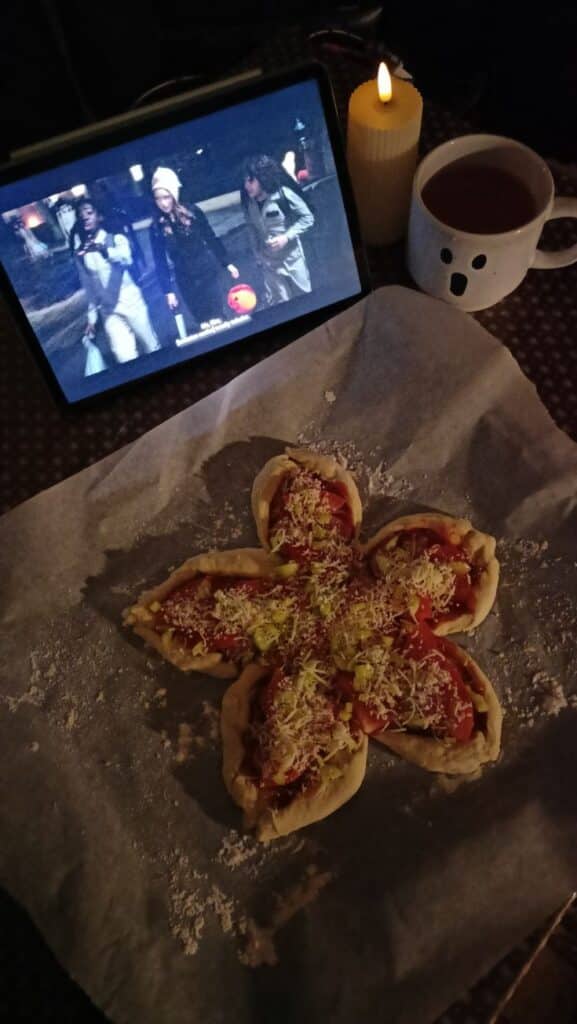 stranger things 💋 - Demogorgon Pizza Recipe: Stranger Things Food Fun Cozy setup with pizza, tablet playing a show, candle, and ghost mug on a table.