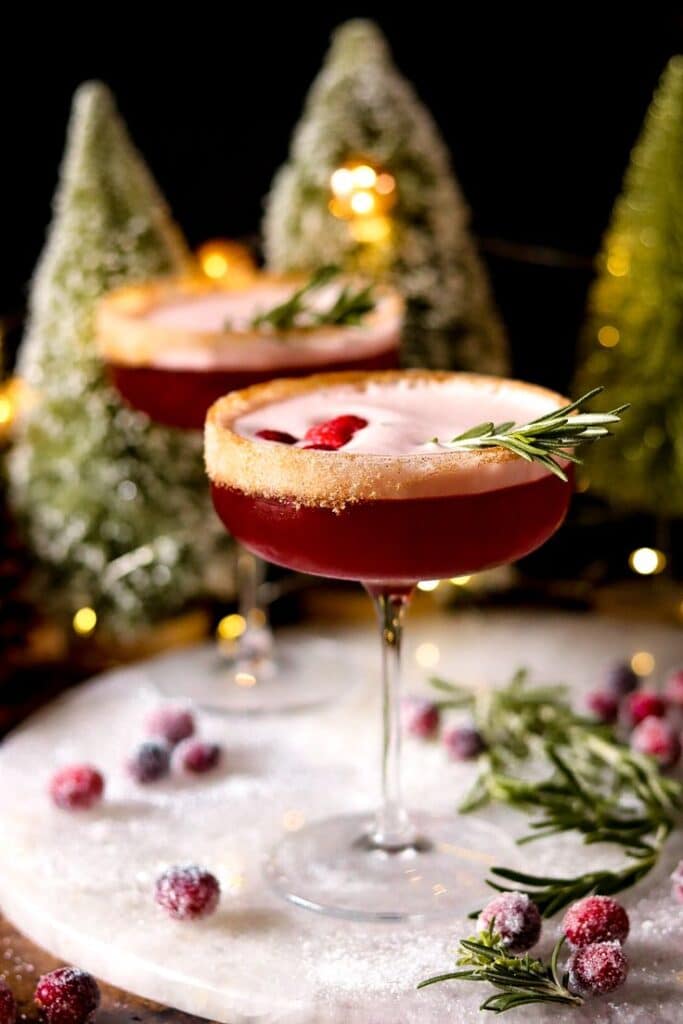 the snowy poinsettia martini - Snowy Poinsettia Martini: Your Ultimate Holiday Cocktail Festive holiday cocktails with cranberry, rosemary garnish, and sugared rim, surrounded by faux snowy trees.