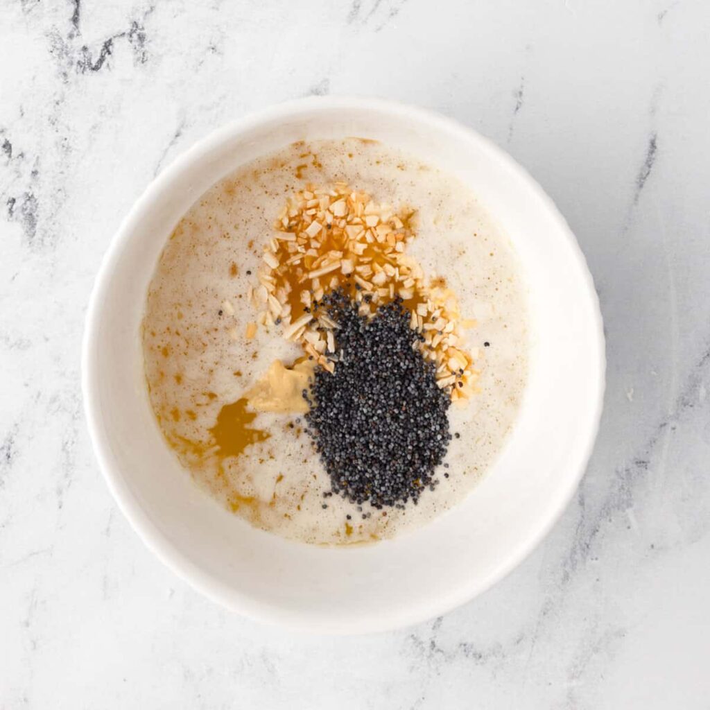 Bowl of poppy seeds, chopped nuts, and batter on a marble counter, ready for baking recipes.