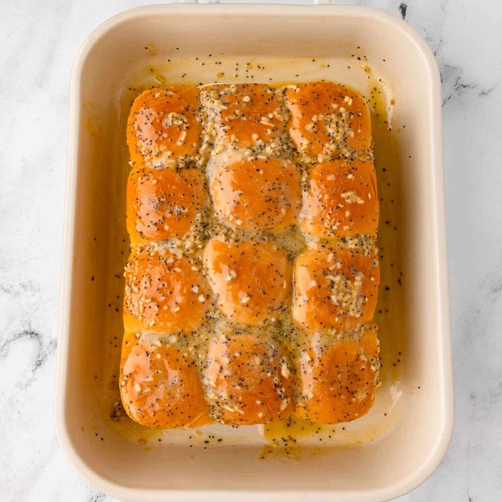 Golden dinner rolls topped with garlic butter and poppy seeds in a baking dish.