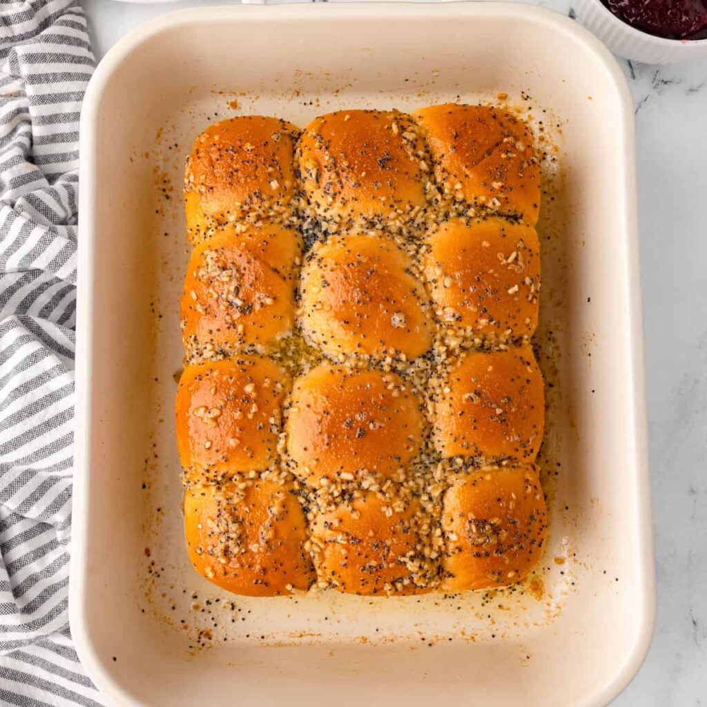 Golden dinner rolls topped with poppy seeds and seasoning in a baking dish, ready to serve.