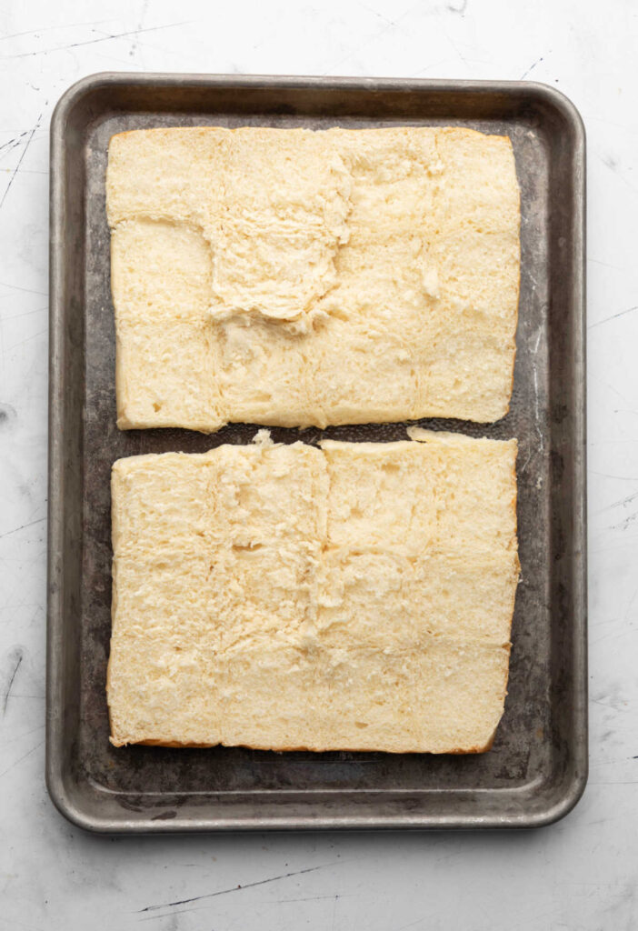 Unbaked sheet of two large sections of fluffy dinner rolls on a metal baking tray.
