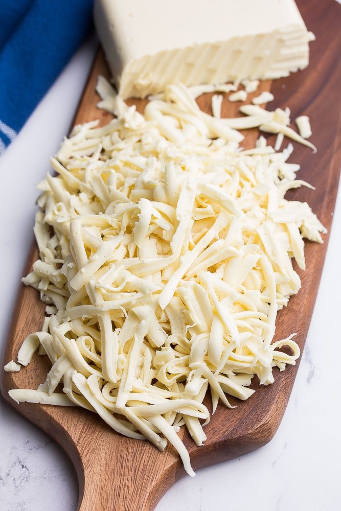 Freshly shredded cheese on a wooden board with a block of cheese, ready for cooking or snacking.