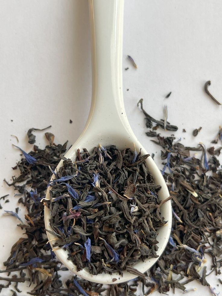 Spoon filled with loose leaf black tea and blue petals isolated on white background.