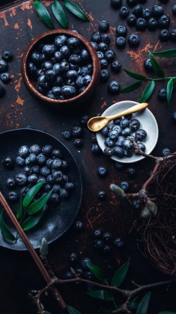 Fresh blueberries in wooden and ceramic bowls with green leaves on a rustic table.