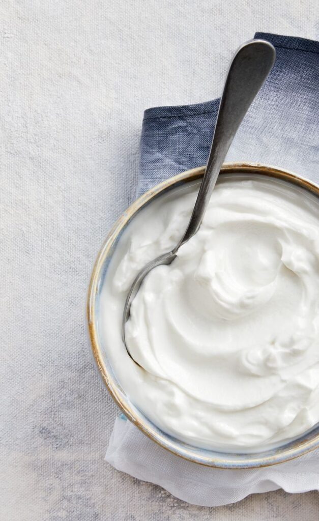 Creamy yogurt in a bowl with a spoon on a gray cloth background. Perfect for breakfast or a healthy snack.
