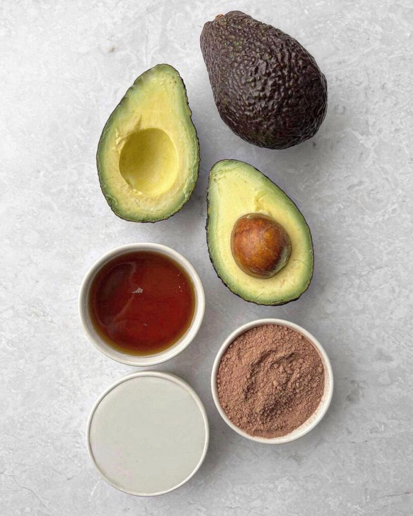 Avocado, honey, and cocoa powder on a countertop, ingredients for a healthy dessert recipe.