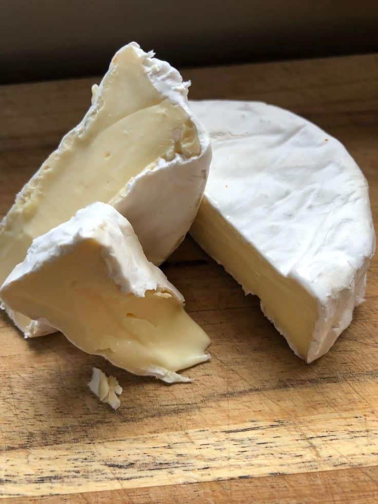 _ 61 - Melted Brie with Honey & Pistachios in 20 Minutes Creamy Brie cheese wedges on a wooden board, showcasing its soft, creamy interior and edible rind.