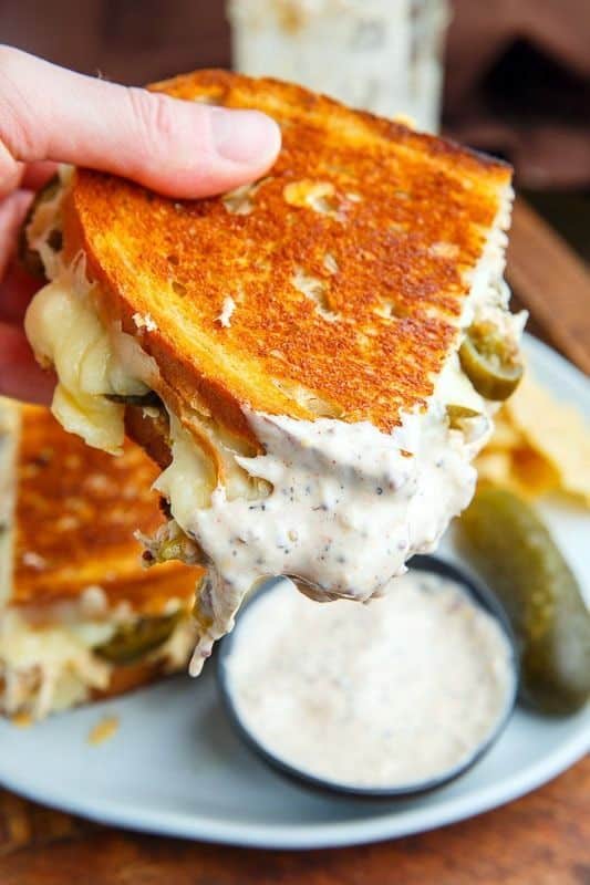 Close-up of a grilled cheese sandwich with creamy dip, featuring crispy bread and melted cheese, held by a hand.