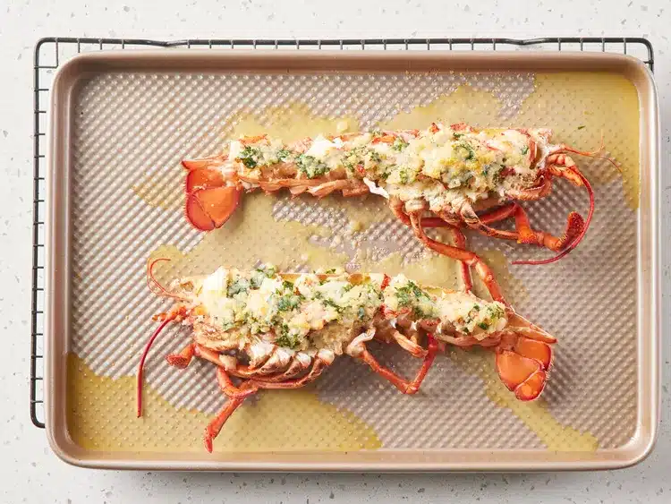 Baked lobster tails with garlic butter and herbs on a baking sheet, ready to serve.
