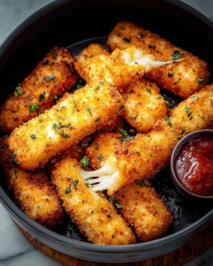 Crispy mozzarella sticks with marinara sauce in a bowl, garnished with herbs. Ideal savory snack close-up.