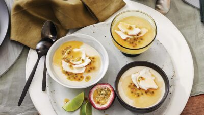 Creamy panna cotta topped with passion fruit and coconut on a speckled plate, garnished with lime slices.