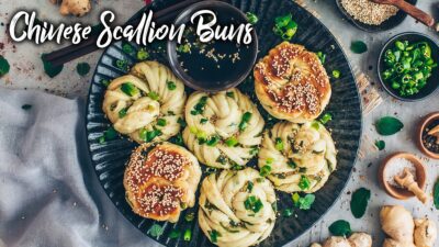 Plate of Chinese scallion buns garnished with sesame seeds and spring onions, served with dipping sauce.