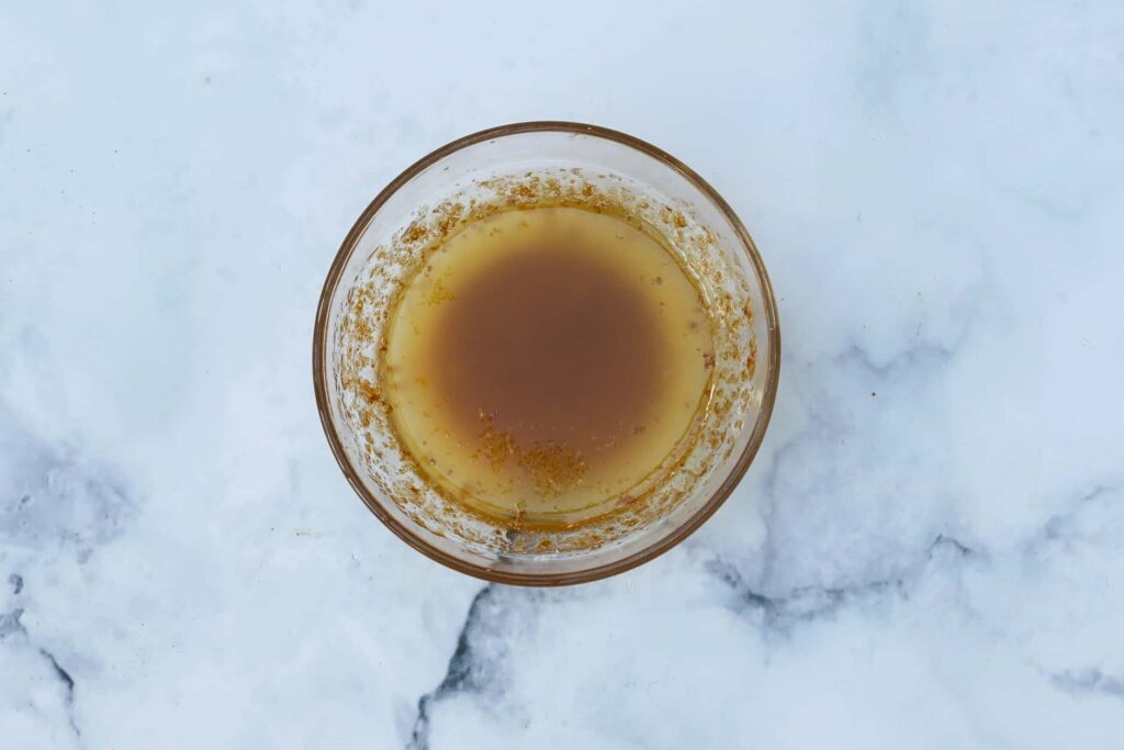 BD2A8774 1 - Enjoy a French Favorite: Sole Meunière & Potatoes Glass bowl with brown liquid on a white marble surface.