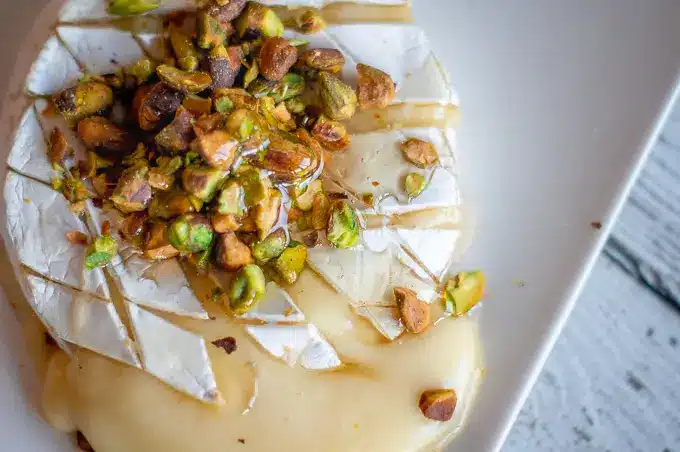 Baked-Brie-with-Honey-Pistachios-3jpg - Melted Brie with Honey & Pistachios in 20 Minutes Melted brie cheese topped with honey and chopped pistachios on a white plate.