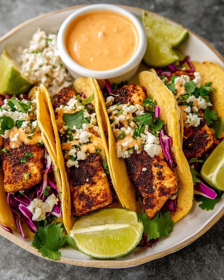 Delicious grilled fish tacos with lime, topped with spicy sauce, cheese, and cilantro on a plate. Perfect taco Tuesday!