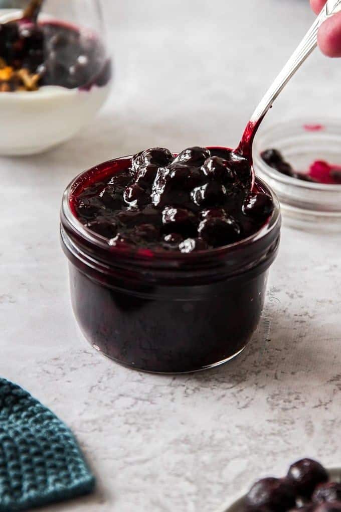 Jar of blueberry compote with spoon, perfect for desserts and breakfast toppings.