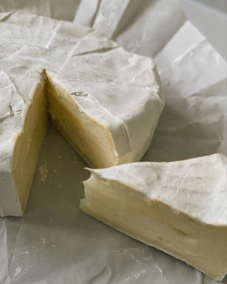 Brie - Melted Brie with Honey & Pistachios in 20 Minutes Creamy Brie cheese wheel with a slice cut out, showing soft interior on parchment paper.