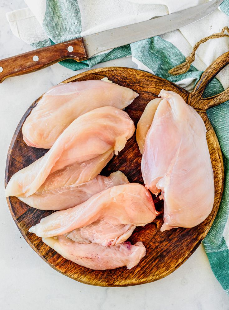 Raw chicken breasts on a wooden cutting board with a knife and cloth napkin, ready for cooking preparation.