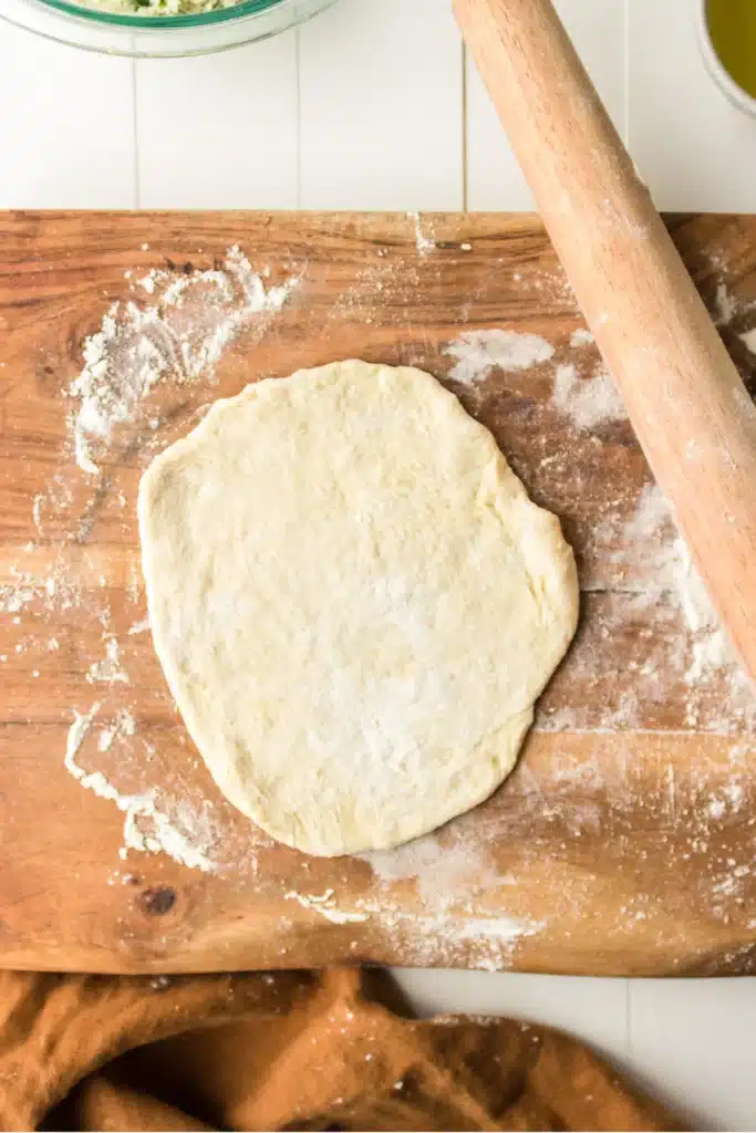 Pizza dough rolled out on a floured wooden board with a rolling pin nearby.