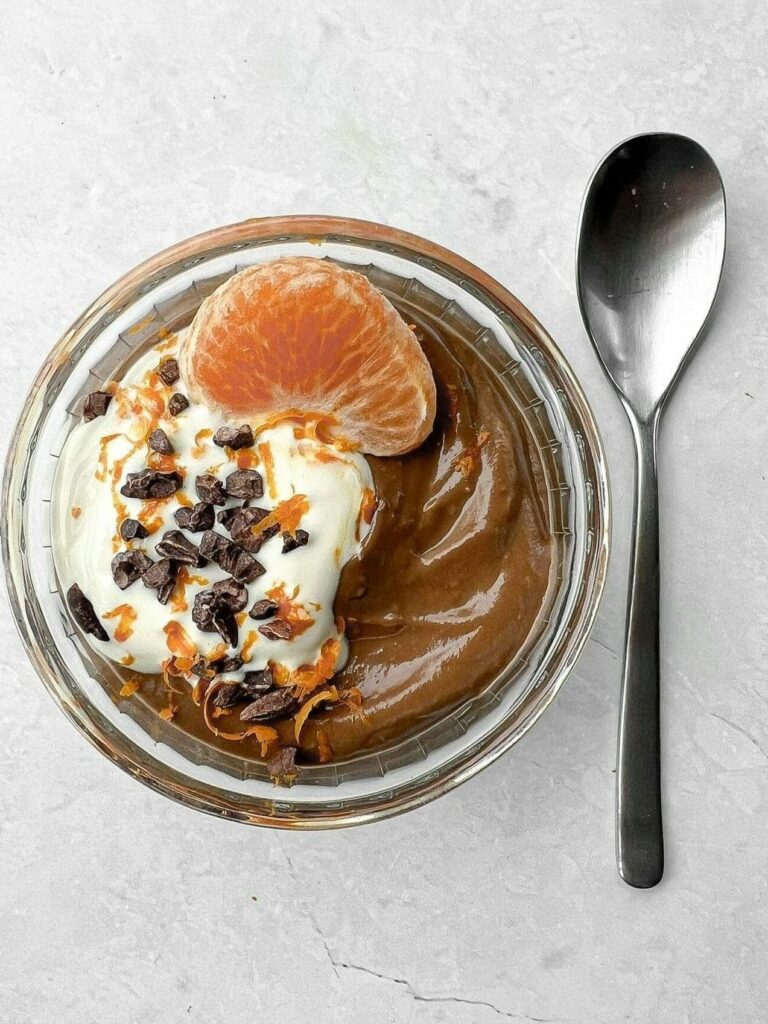 Creamy chocolate mousse topped with whipped cream, orange slice, and cacao nibs, served with a spoon.