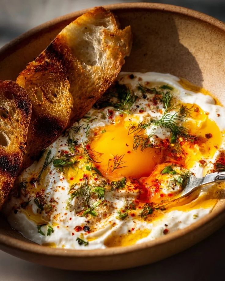 Poached egg with spiced yogurt and herbs in a bowl, served with crusty bread.