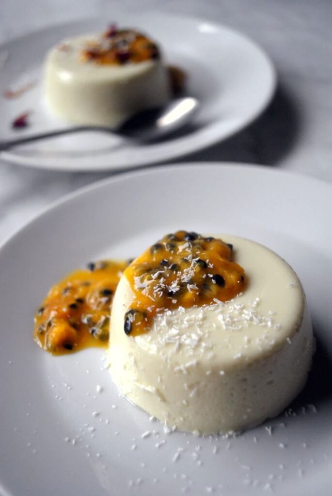 Coconut and Passion Fruit Panna Cottas - From France With Love - Silky, Tropical Coconut & Passion Fruit Panna Cotta Creamy panna cotta topped with fresh passion fruit and coconut on a white plate. Elegant dessert presentation.
