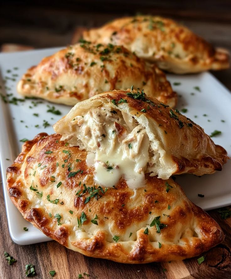 Golden brown empanadas with melted cheese and herbs on a white plate, wooden background.