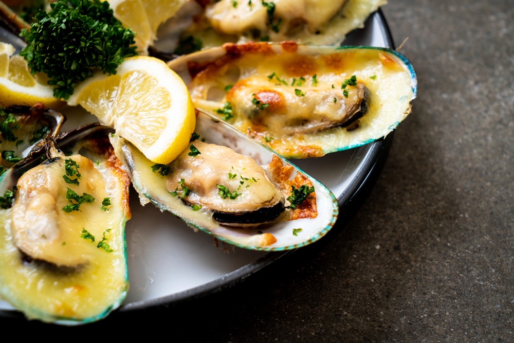 Baked mussels with cheese, garnished with parsley and lemon wedges on a plate; a savory seafood dish.